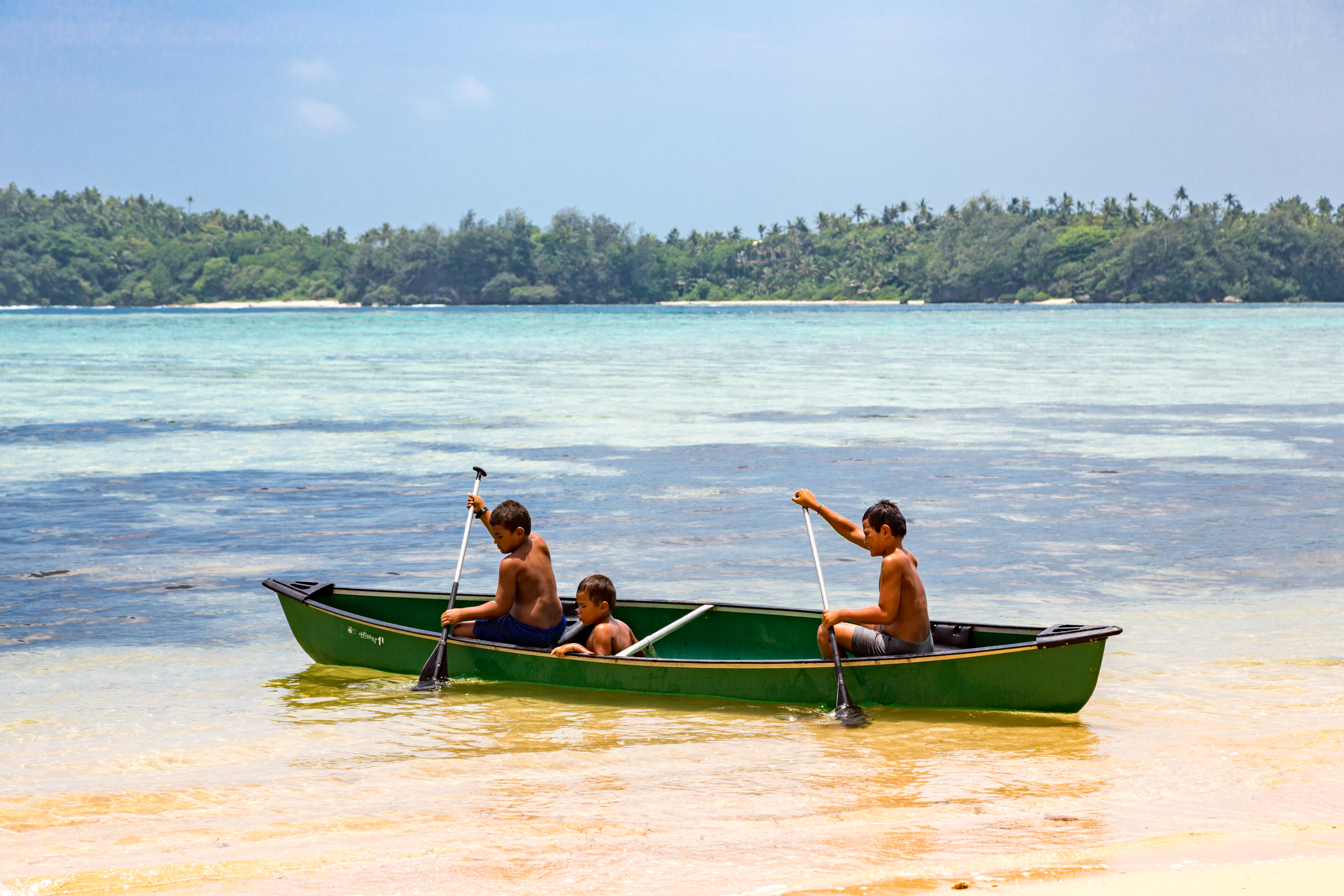 Three boys row a canoe in Tonga