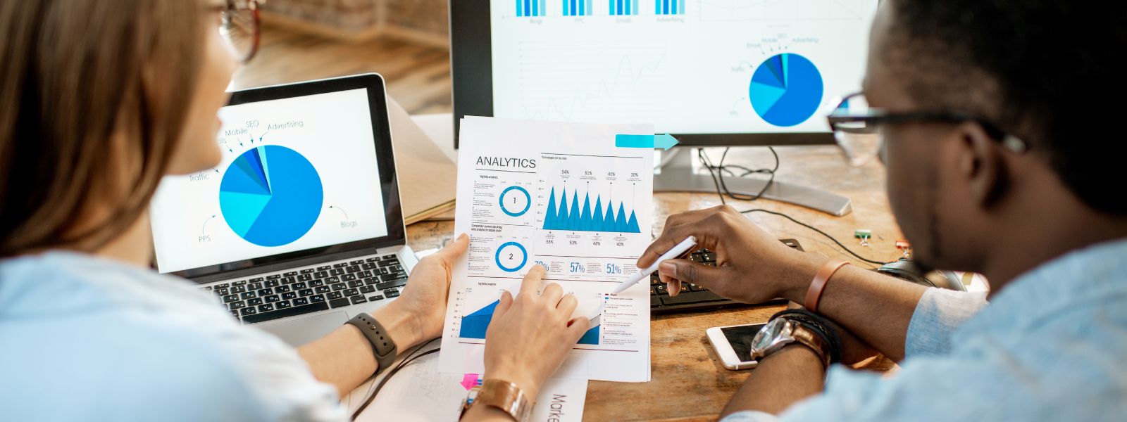 A woman and man study analytics at a desk with computers