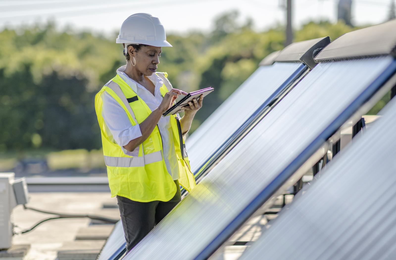 Woman in a hard hart writing on a pad next to solar panels