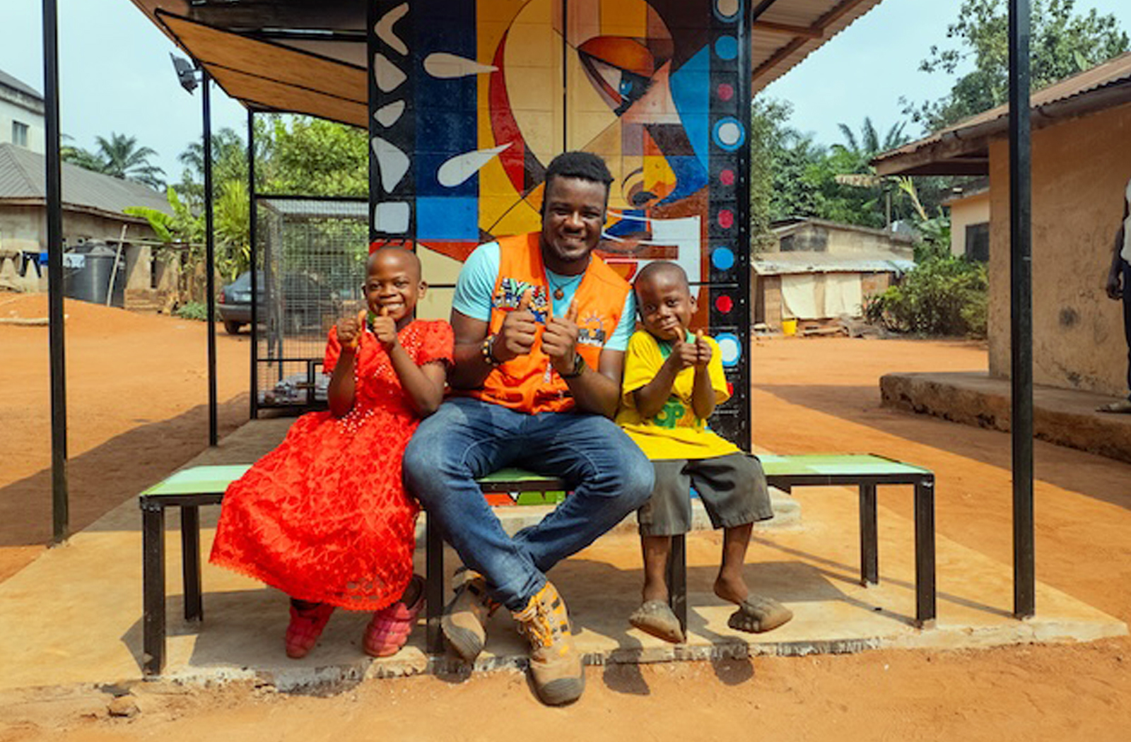 Stanley Anigbogu with a young girl and boy sitting by a solar charging station