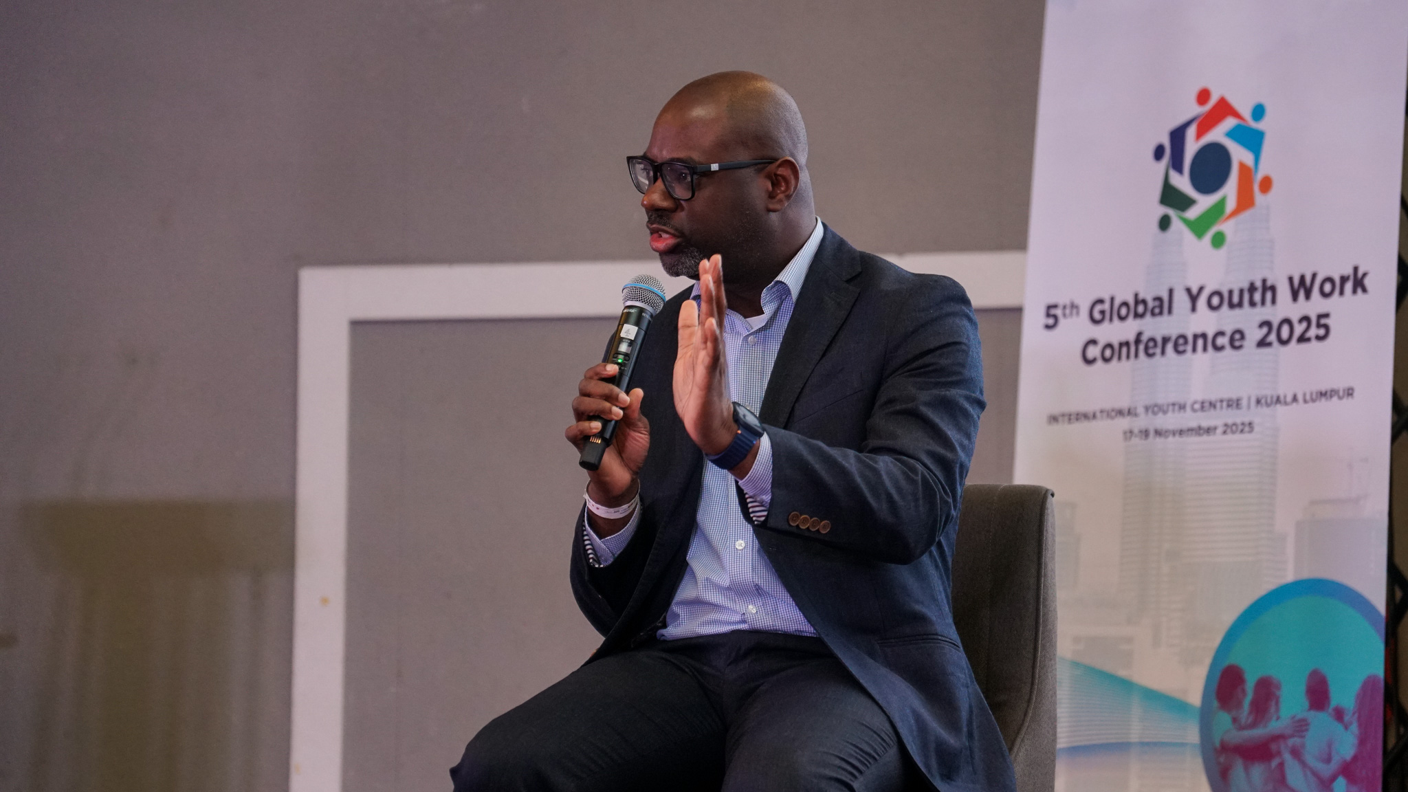 Layne Robinson, Layne Robinson, Head of Social Policy Development at the Commonwealth Secretariat, speaks into a microphone on stage at the Global Youth Work Conference in Malaysia