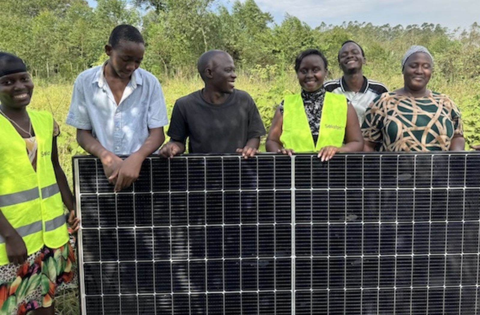 Shifra and group of smallholder farmers stand behind a solar panel