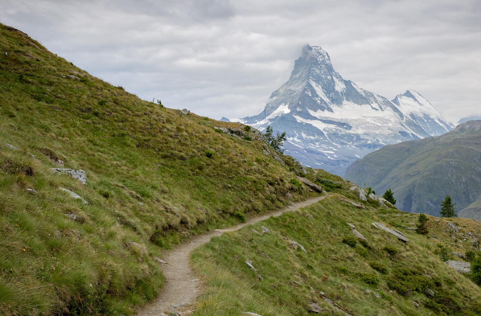 A photograph of a narrow hillside path leading to a tall mountain (the Matterhorn on the Italian-Swiss border)