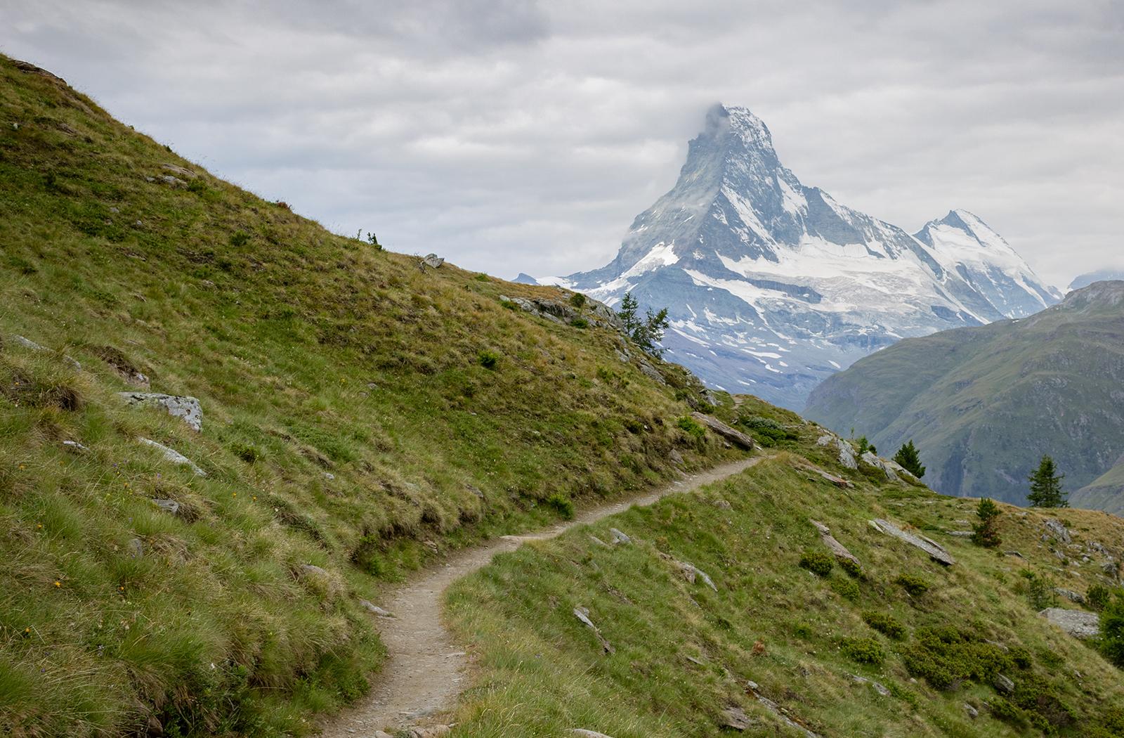 A photograph of a narrow hillside path leading to a tall mountain (the Matterhorn on the Italian-Swiss border)
