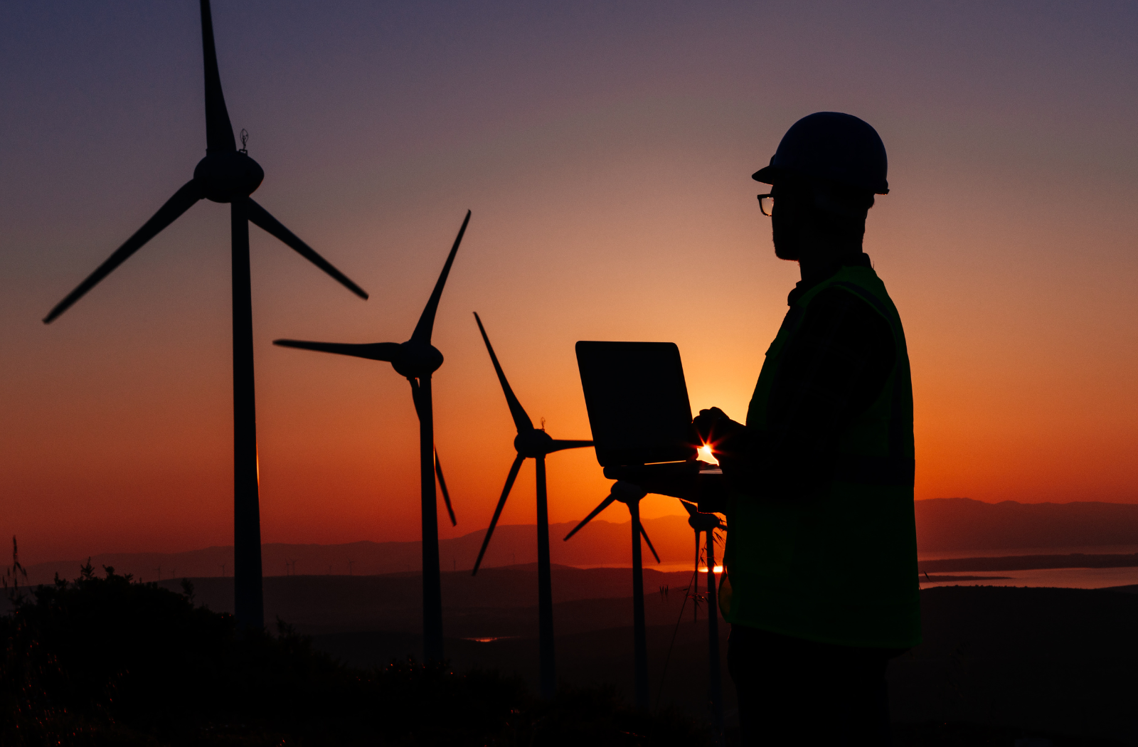 Clean energy being generated by wind turbines in a field at sunset supervised by operative with a laptop.