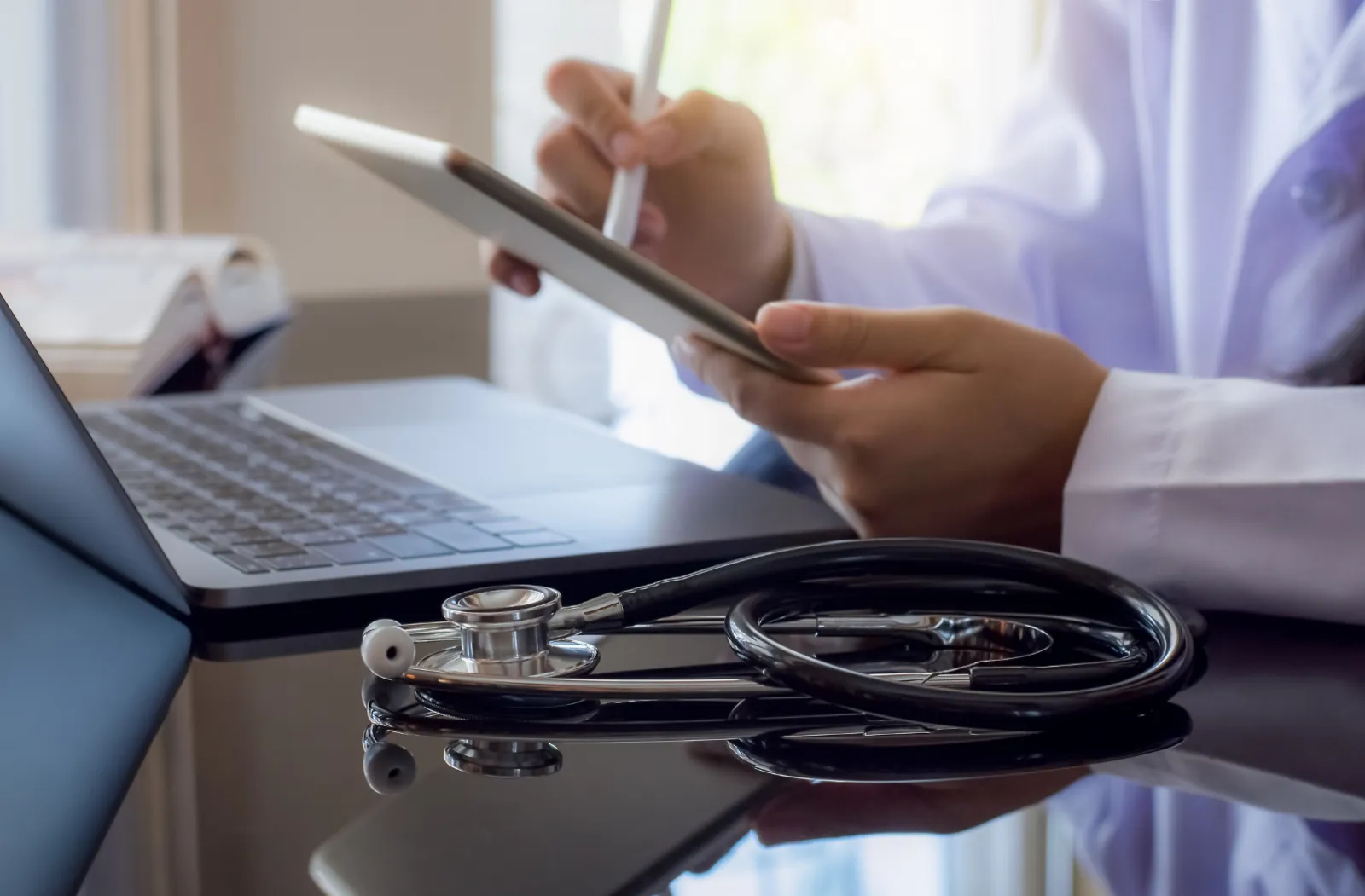 A doctor looking uses a tablet next to a laptop