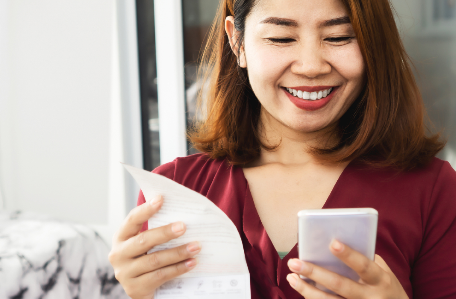 Woman smiling holding a phone and a bill to pay