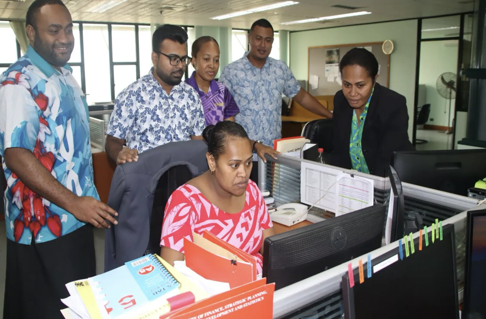 People gather around a computer in an office