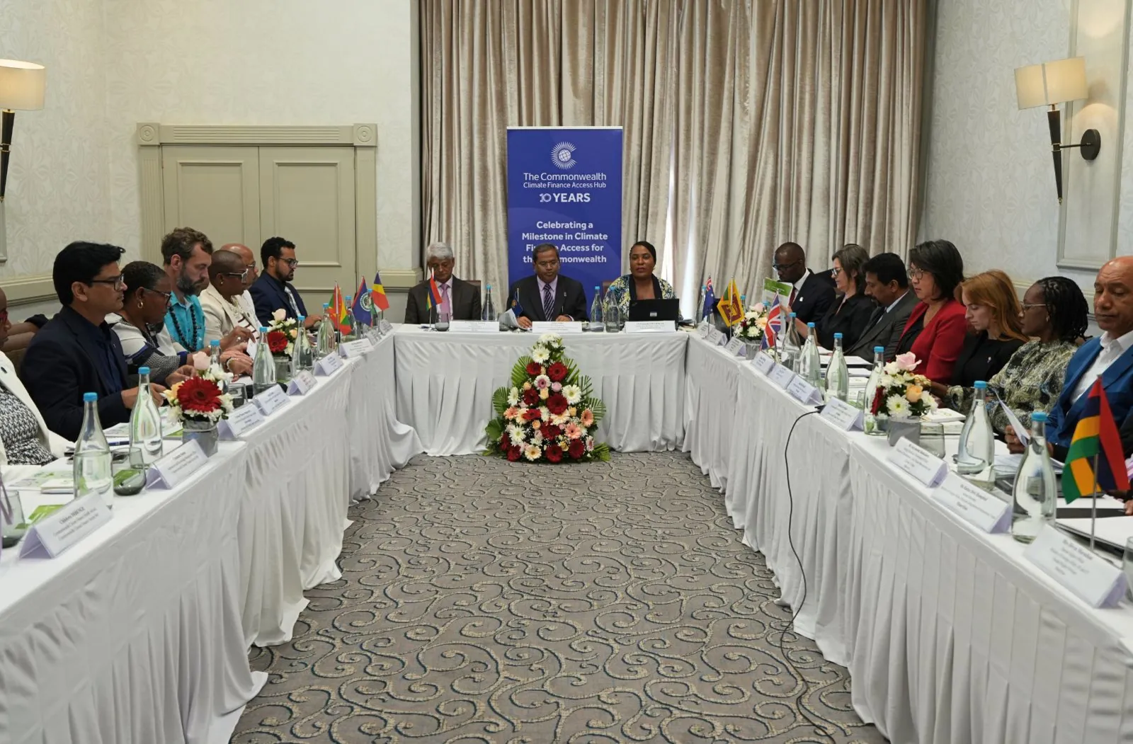 People sitting around the table for a Commonwealth Climate Finance Access Hub Steering Committee meeting with a banner in the background