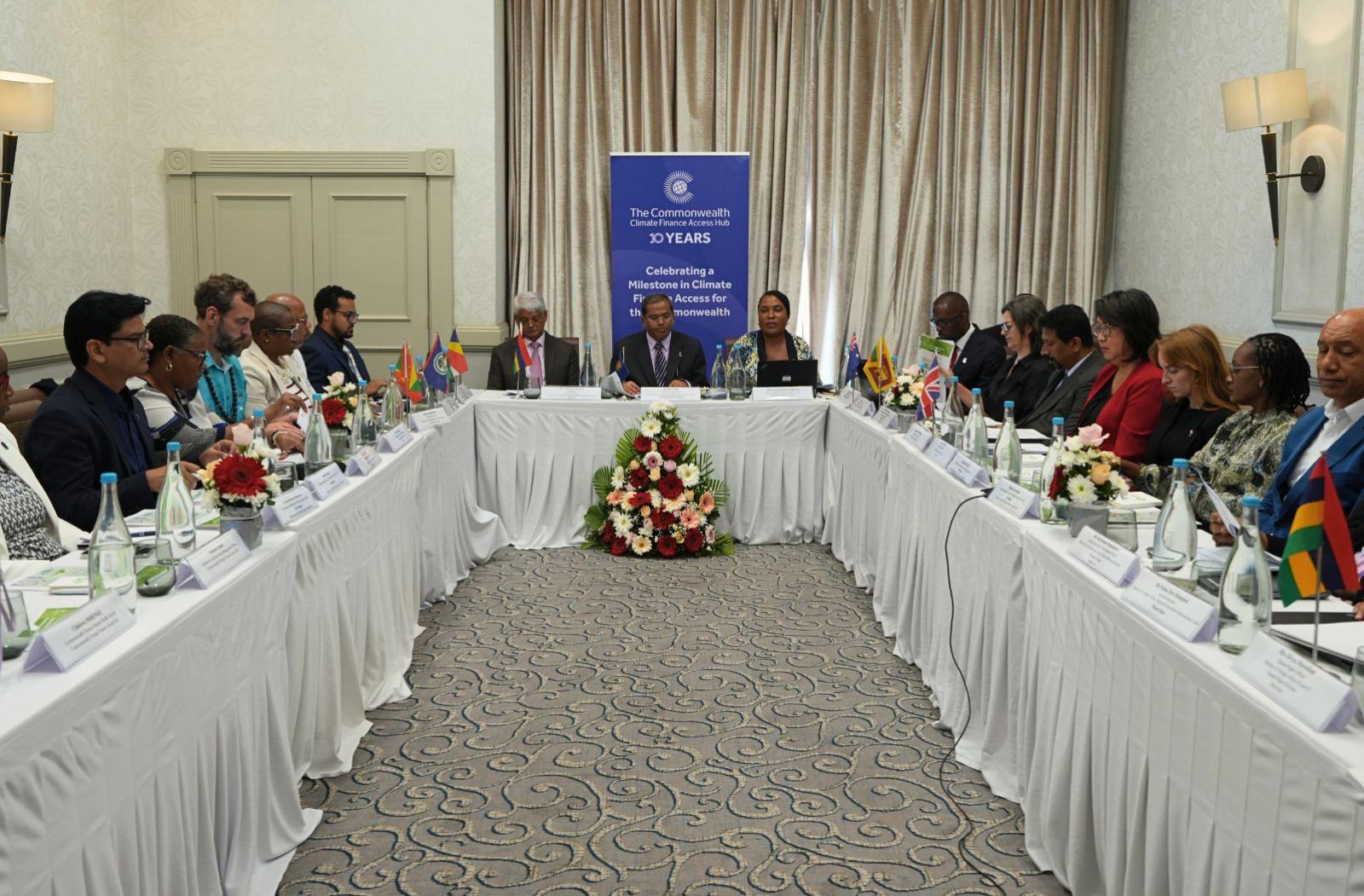 People sitting around the table for a Commonwealth Climate Finance Access Hub Steering Committee meeting with a banner in the background 