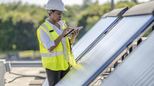 Woman in a hard hart writing on a pad next to solar panels