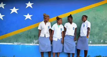 Four students stand in front of a mural of the flag of Solomon Islands.