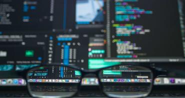 reading glasses in front of monitors displaying financial data