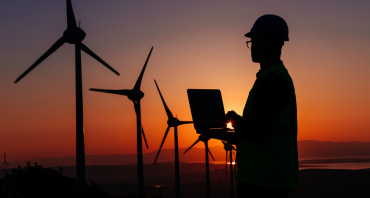 Clean energy being generated by wind turbines in a field at sunset supervised by operative with a laptop.
