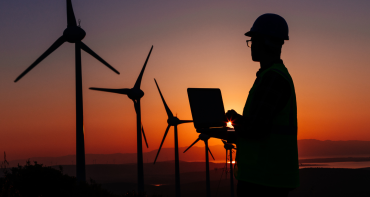 Clean energy being generated by wind turbines in a field at sunset supervised by operative with a laptop.
