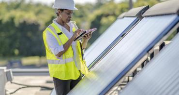 Woman in a hard hart writing on a pad next to solar panels