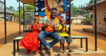 Stanley Anigbogu with a young girl and boy sitting by a solar charging station