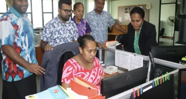 People gather around a computer in an office