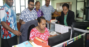 People gather around a computer in an office