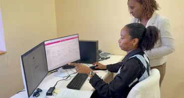 Two officials in Saint Lucia's Ministry of Finance look at the Commonwealth Meridian system on two computer screens