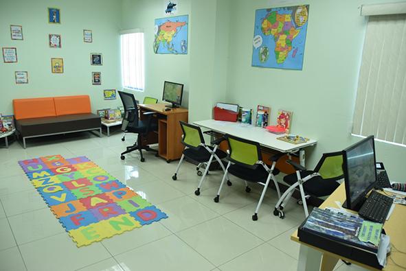 A children's holding room featuring a play mat, tables and desks and a variety of materials and resources for children